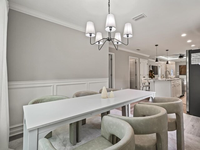 dining room with ceiling fan with notable chandelier, ornamental molding, sink, and light hardwood / wood-style flooring