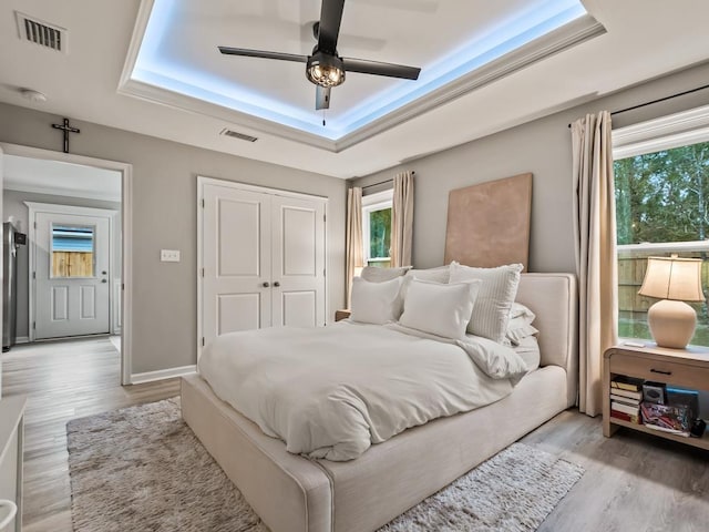 bedroom featuring a tray ceiling, multiple windows, ceiling fan, and light hardwood / wood-style floors