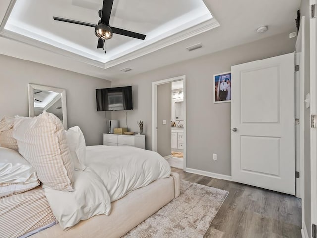 bedroom featuring ceiling fan, a raised ceiling, light wood-type flooring, and ensuite bathroom