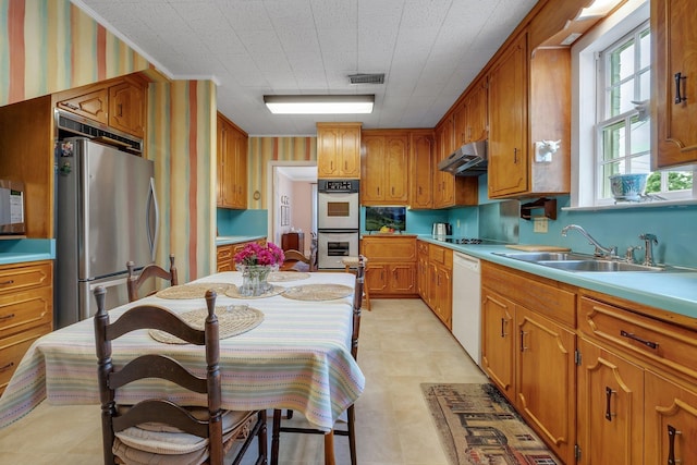 1540 Isabel Ct, Tallahassee, FL 32303 - kitchen with stainless steel appliances, under cabinet range hood, brown cabinets, wallpapered walls, and light countertops
