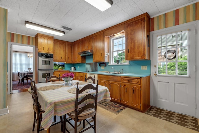 1540 Isabel Ct, Tallahassee, FL 32303 - kitchen featuring double oven, brown cabinets, light countertops, under cabinet range hood, and wallpapered walls