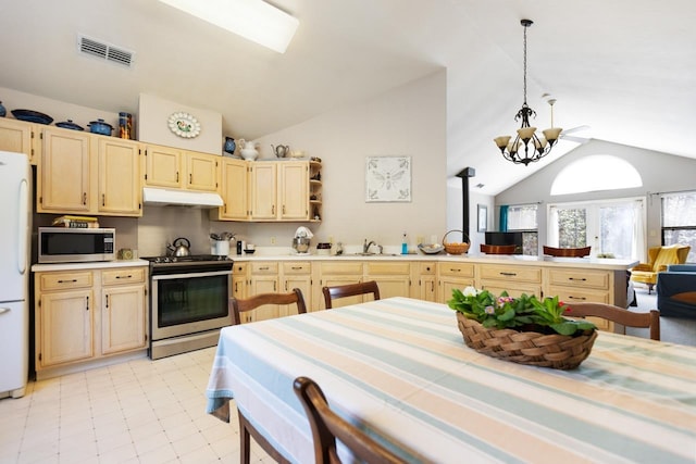 kitchen featuring appliances with stainless steel finishes, light brown cabinetry, decorative light fixtures, lofted ceiling, and an inviting chandelier