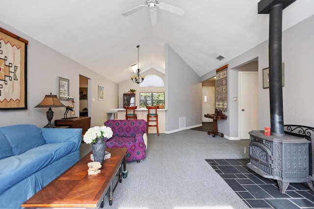 living room with dark colored carpet, vaulted ceiling, a wood stove, and ceiling fan with notable chandelier