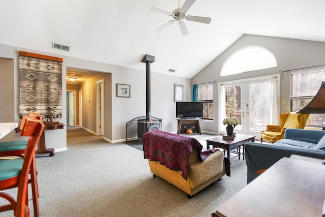 carpeted living room with high vaulted ceiling, a wood stove, ceiling fan, and french doors