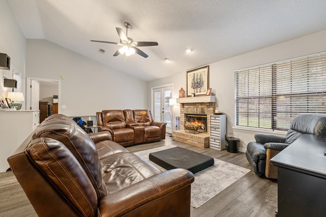 living room featuring a textured ceiling, lofted ceiling, wood-type flooring, a fireplace, and ceiling fan