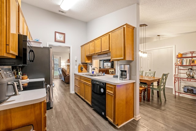 kitchen with pendant lighting, sink, light wood-type flooring, a textured ceiling, and black dishwasher