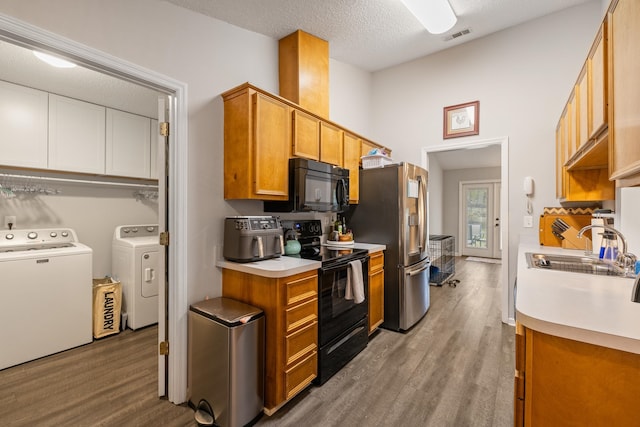 kitchen with a textured ceiling, black appliances, washing machine and dryer, sink, and light wood-type flooring