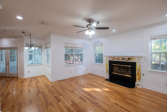 unfurnished living room with ceiling fan with notable chandelier, light wood-type flooring, plenty of natural light, and crown molding