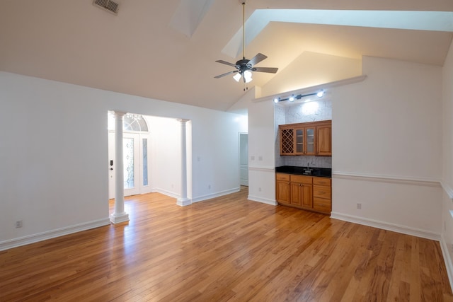 unfurnished living room featuring ornate columns, ceiling fan, sink, high vaulted ceiling, and light hardwood / wood-style flooring