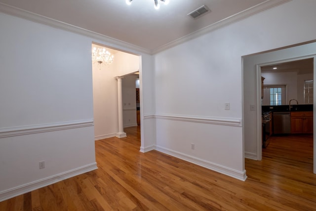 spare room with decorative columns, ornamental molding, sink, a notable chandelier, and light hardwood / wood-style floors