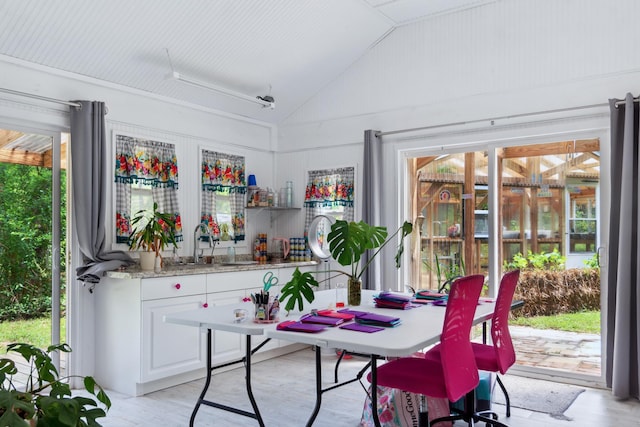 dining space with sink, light hardwood / wood-style flooring, and high vaulted ceiling