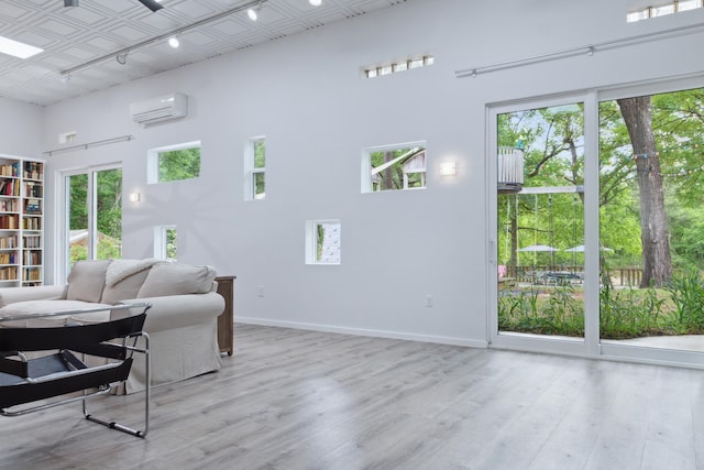 living room featuring an AC wall unit, light wood-type flooring, a wealth of natural light, and a towering ceiling