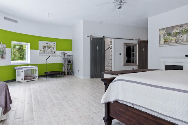 bedroom featuring a barn door, ceiling fan, and light wood-type flooring