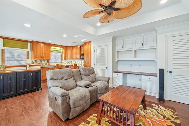 living room featuring light hardwood / wood-style flooring, built in desk, ceiling fan, and a tray ceiling