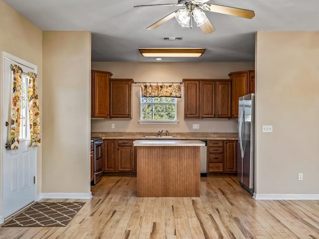 kitchen with a kitchen island, stainless steel appliances, sink, ceiling fan, and light hardwood / wood-style flooring