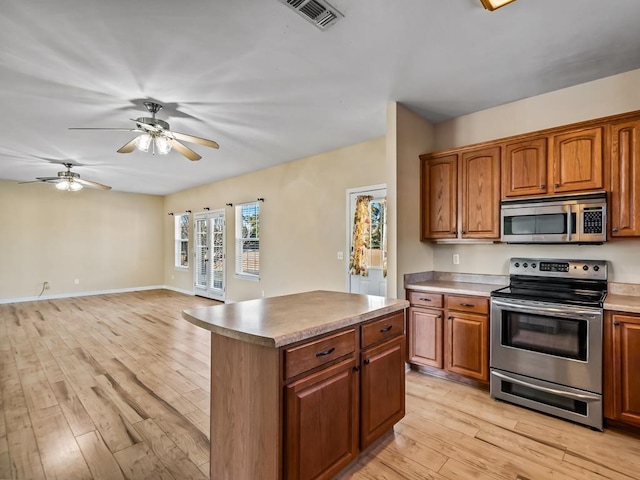 kitchen with ceiling fan, appliances with stainless steel finishes, light hardwood / wood-style flooring, and a kitchen island