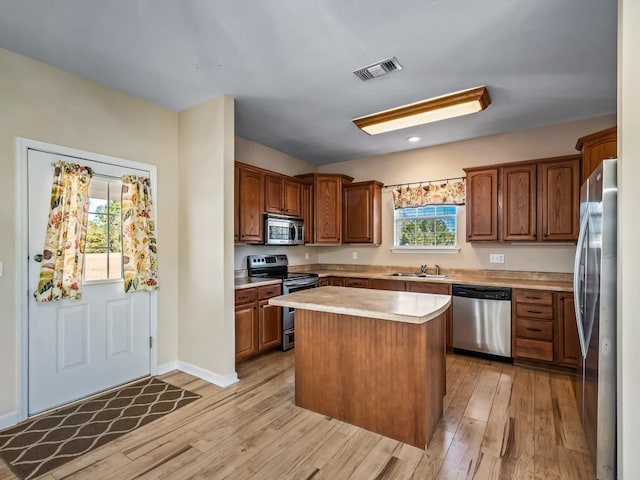 kitchen featuring light wood-type flooring, appliances with stainless steel finishes, a kitchen island, and sink