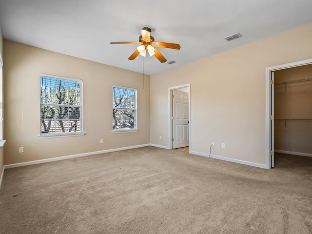 unfurnished bedroom featuring a spacious closet, light colored carpet, a closet, and ceiling fan