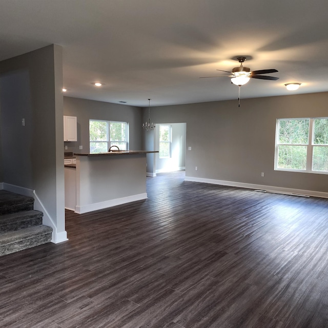 unfurnished living room featuring ceiling fan with notable chandelier and dark hardwood / wood-style flooring