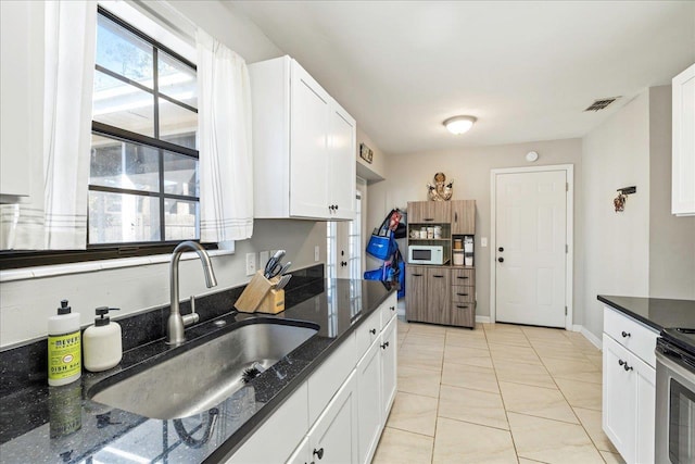 kitchen featuring light tile patterned floors, white cabinetry, dark stone countertops, and sink