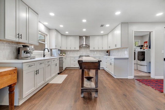 kitchen with dishwasher, wall chimney exhaust hood, light countertops, washing machine and dryer, and white cabinetry