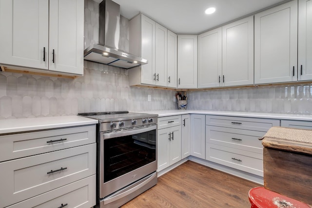 kitchen featuring stainless steel electric stove, light countertops, backsplash, white cabinets, and wall chimney exhaust hood