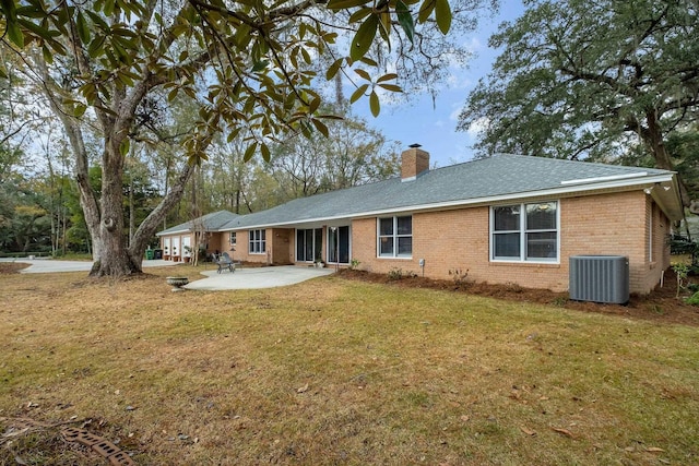 rear view of property featuring brick siding, a chimney, central air condition unit, a lawn, and a patio area