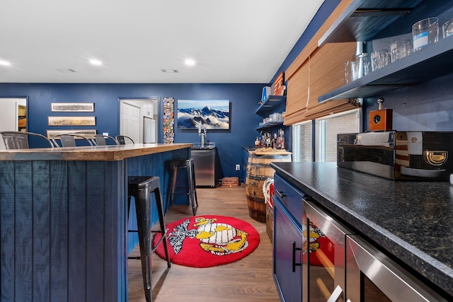 kitchen with beverage cooler, dark countertops, a breakfast bar, light wood-style floors, and open shelves