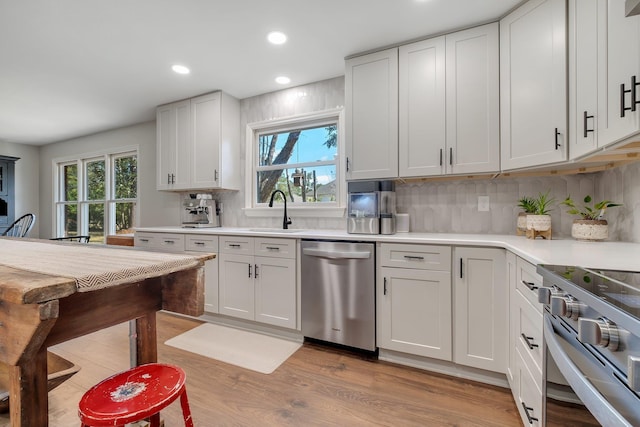 kitchen featuring light countertops, decorative backsplash, appliances with stainless steel finishes, white cabinets, and a sink