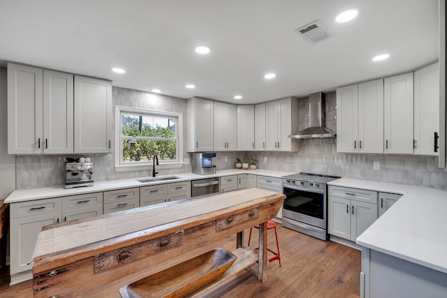 kitchen with stainless steel appliances, a sink, visible vents, light countertops, and wall chimney range hood