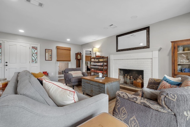 living room featuring a brick fireplace, wood finished floors, visible vents, and recessed lighting