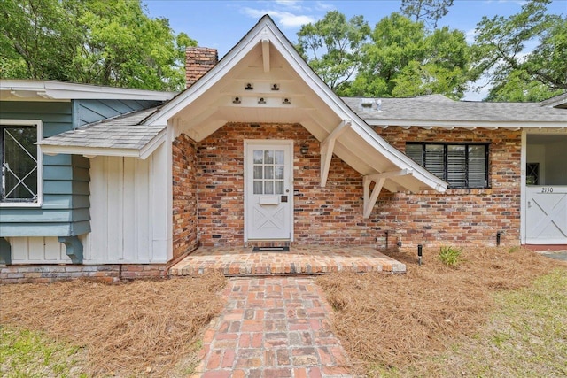 view of exterior entry with a chimney, roof with shingles, board and batten siding, and brick siding