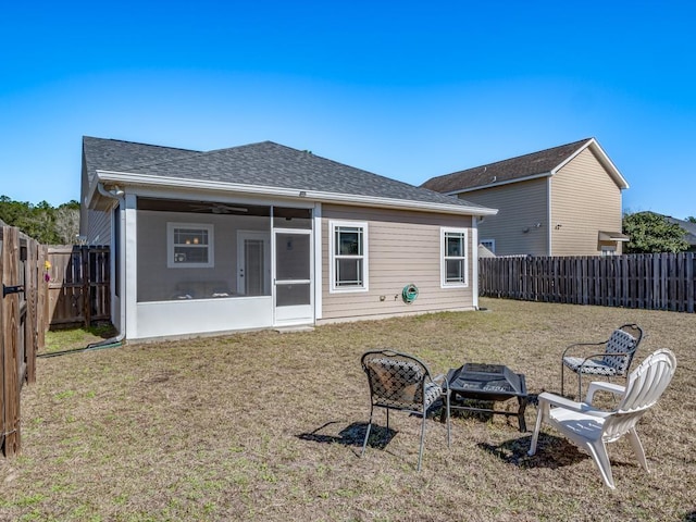 rear view of property featuring an outdoor fire pit, a sunroom, a fenced backyard, roof with shingles, and a yard