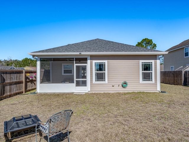 rear view of property featuring a sunroom, a fenced backyard, a shingled roof, and a yard