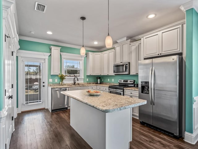 kitchen with a sink, light countertops, appliances with stainless steel finishes, hanging light fixtures, and a center island