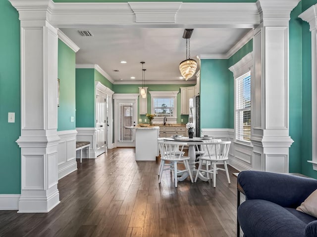 dining space featuring crown molding, dark wood finished floors, visible vents, and decorative columns