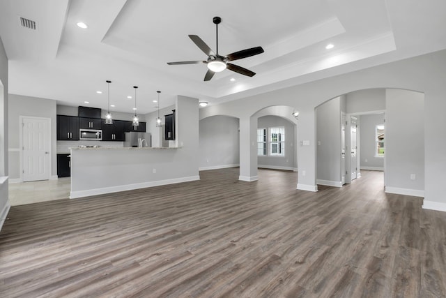 unfurnished living room featuring a tray ceiling, ceiling fan, dark hardwood / wood-style flooring, and a healthy amount of sunlight