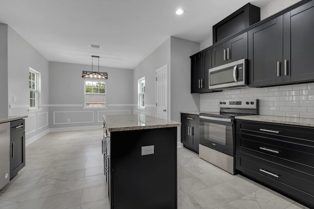 kitchen with light stone countertops, a center island, backsplash, pendant lighting, and appliances with stainless steel finishes