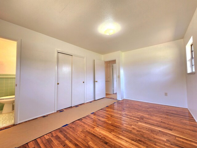 unfurnished bedroom featuring hardwood / wood-style floors, connected bathroom, and a closet