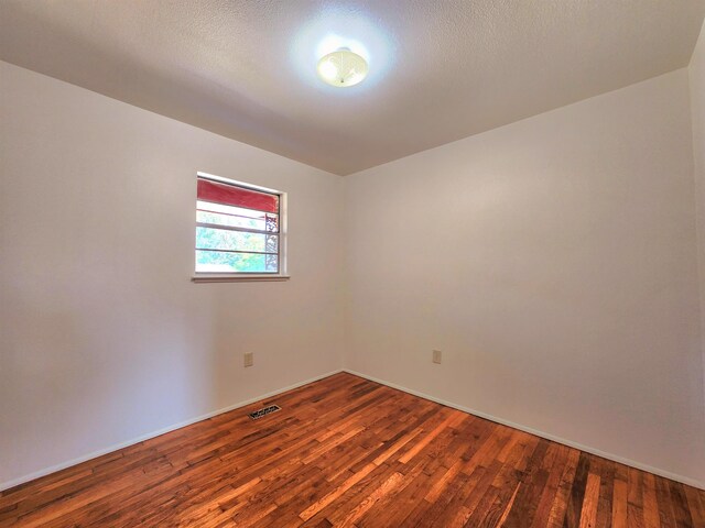 empty room with a textured ceiling and dark hardwood / wood-style flooring