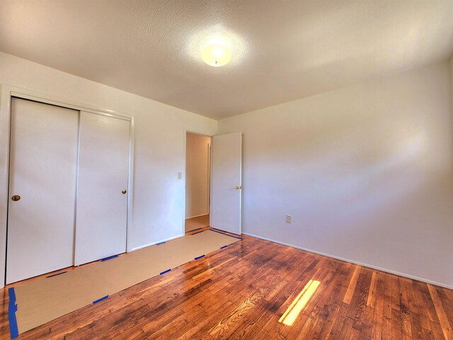 unfurnished bedroom with wood-type flooring, a textured ceiling, and a closet