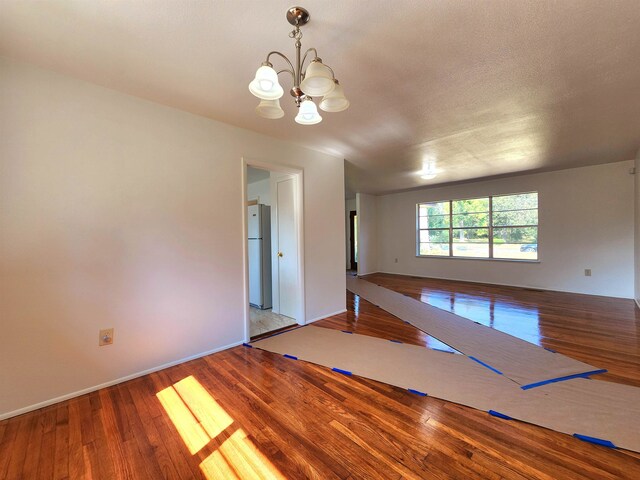 unfurnished room with a textured ceiling, hardwood / wood-style flooring, and a chandelier