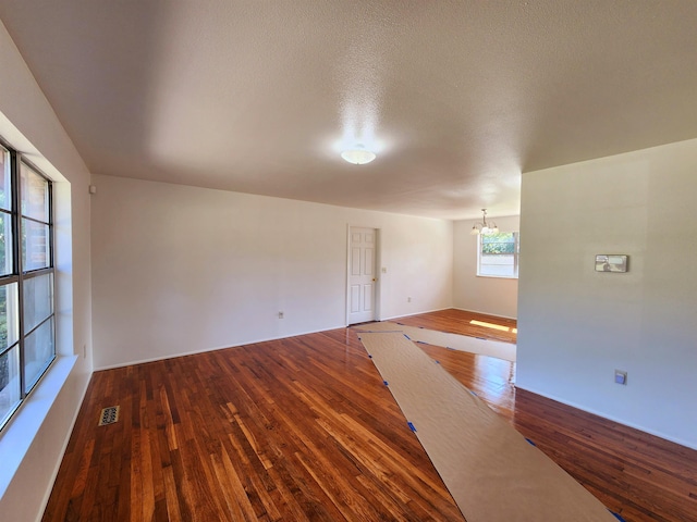 empty room with a textured ceiling, dark hardwood / wood-style floors, and an inviting chandelier