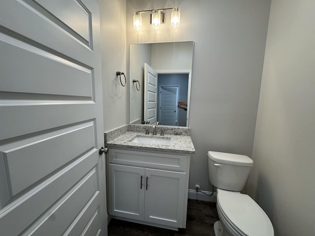 half bath with toilet, baseboards, and vanity