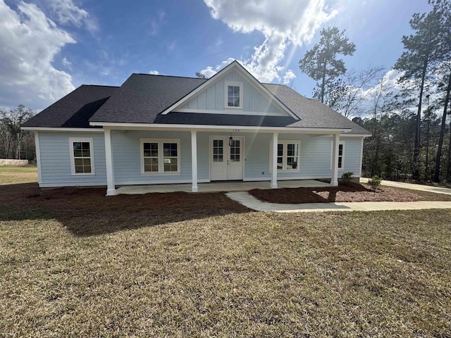 view of front facade with covered porch, french doors, board and batten siding, and a front yard