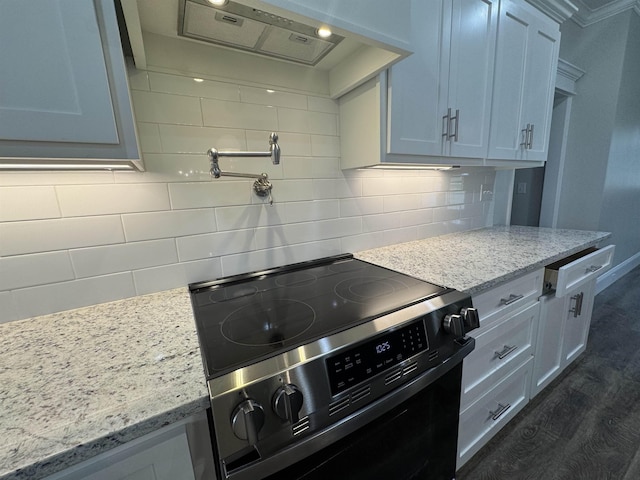 kitchen featuring dark wood-style floors, light stone counters, black electric range, decorative backsplash, and exhaust hood