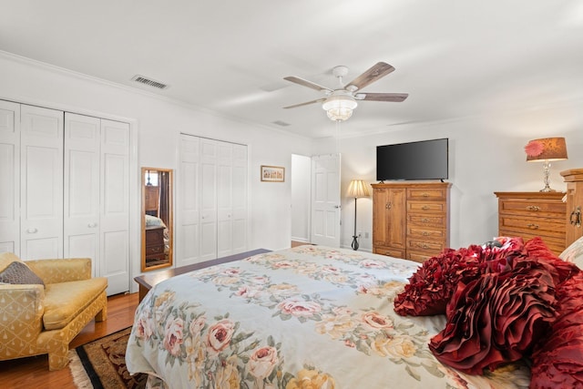 bedroom with multiple closets, wood-type flooring, ornamental molding, and ceiling fan