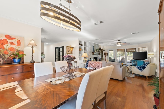 dining room with crown molding, hardwood / wood-style floors, ceiling fan, and a fireplace