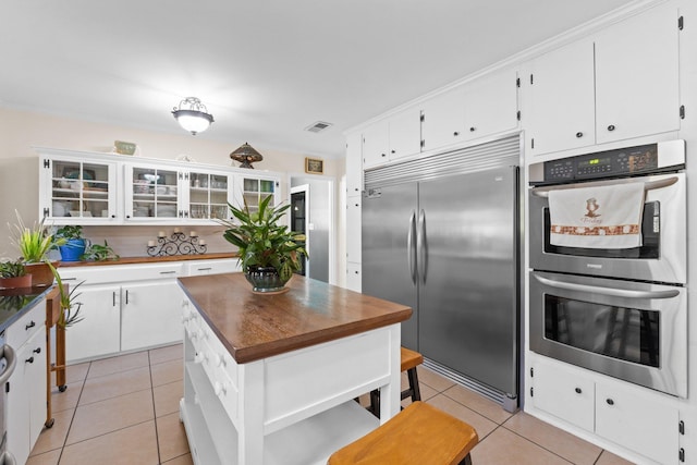 kitchen with stainless steel appliances, light tile patterned floors, a kitchen island, and white cabinets