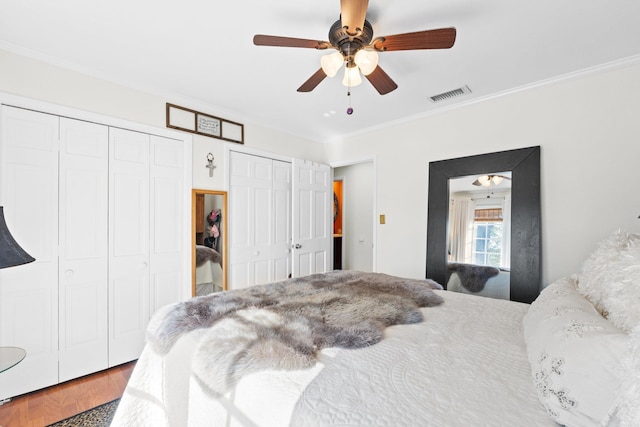 bedroom with crown molding, two closets, wood-type flooring, and ceiling fan